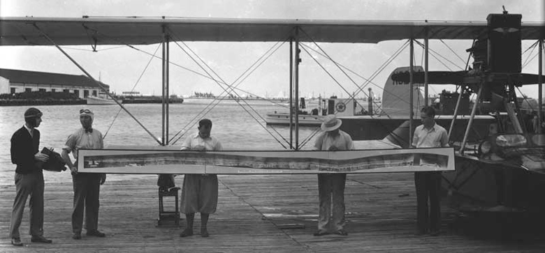 Men hold a composite aerial photograph of the coast. Richard Hoit, one of the region’s first aerial photographers, probably made the composite photograph as well as this view. May 5, 1929. Photo by Richard B. Hoit. HistoryMiami. Hoit C10200.